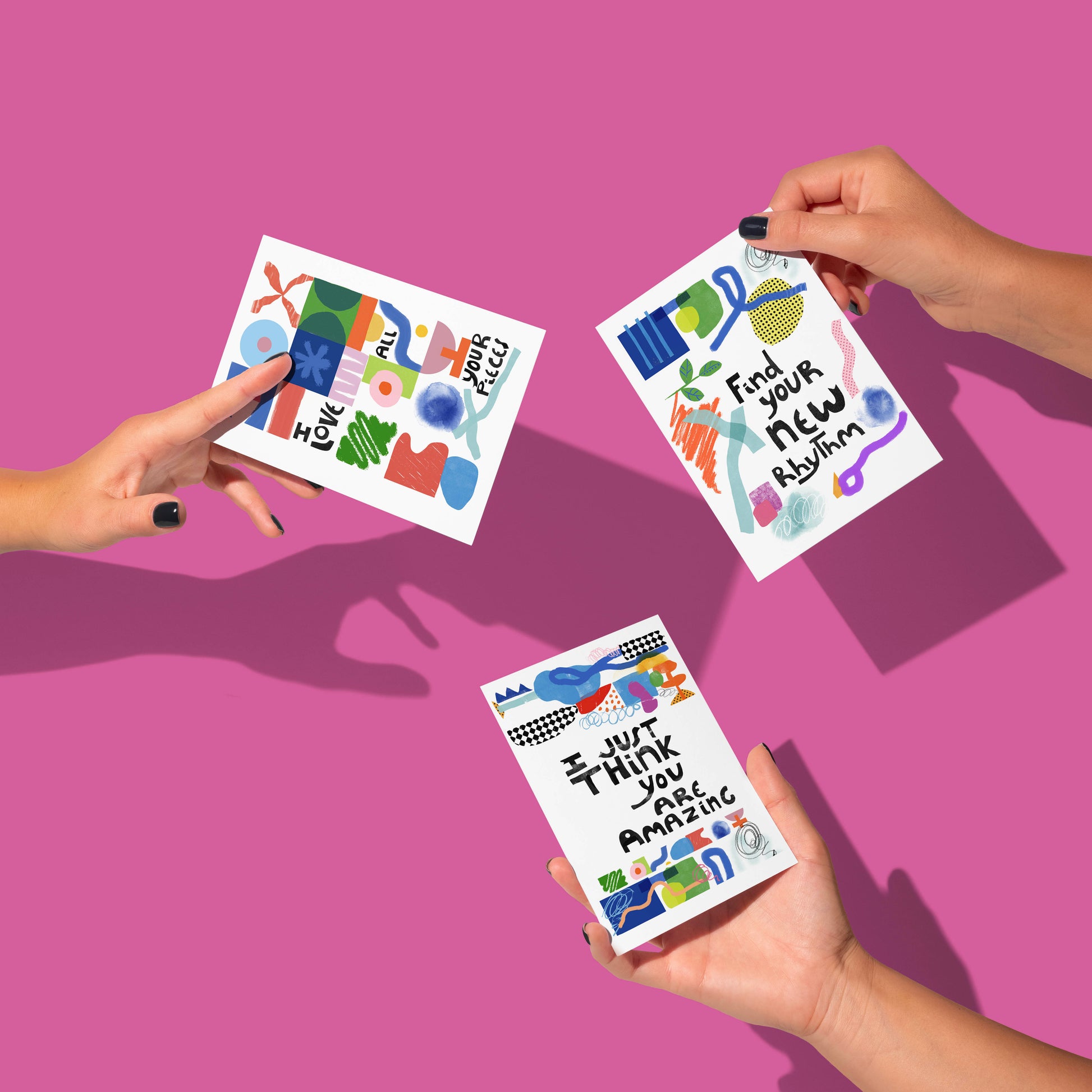 Three hands holding colorful cards with motivational phrases on a pink background