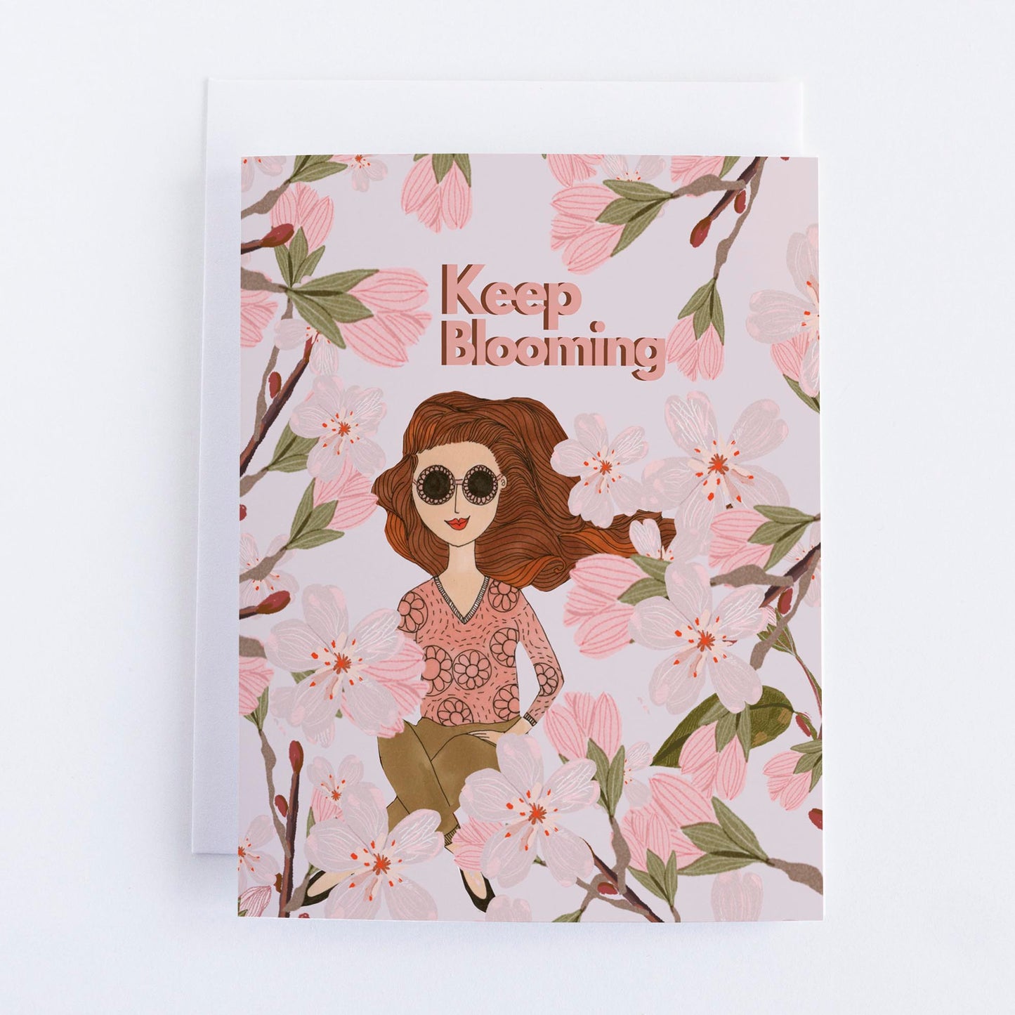A greeting card with an illustration of a person with sunglasses among floral elements, and the text 'Keep Blooming' written above.