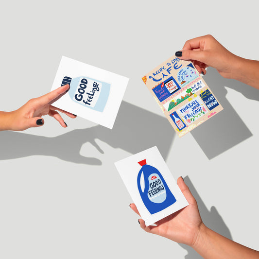 Three colorful greeting cards with text and graphics held by hands on a light gray background