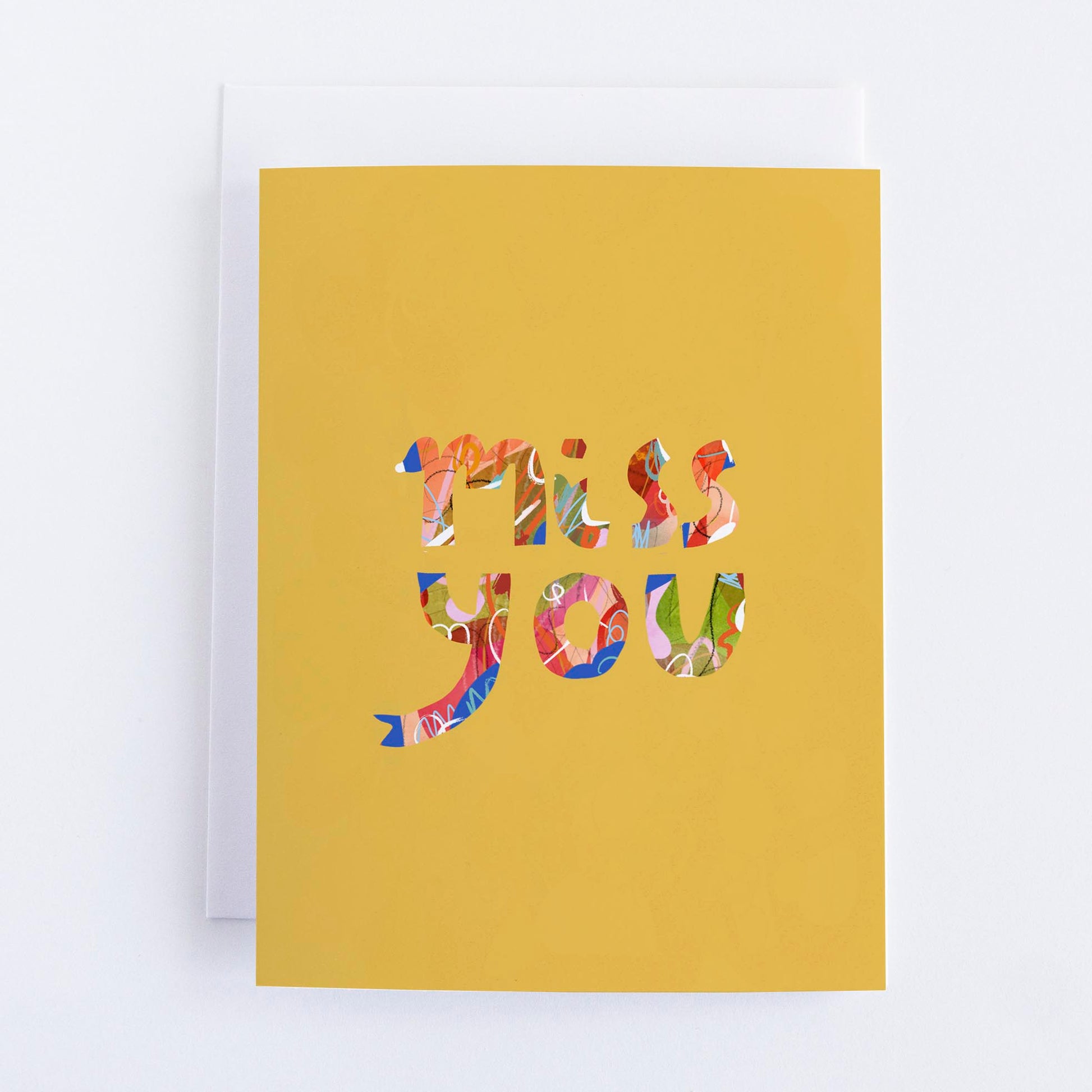 A yellow greeting card with the words 'Miss You' cut out in a colorful pattern from the card's material.