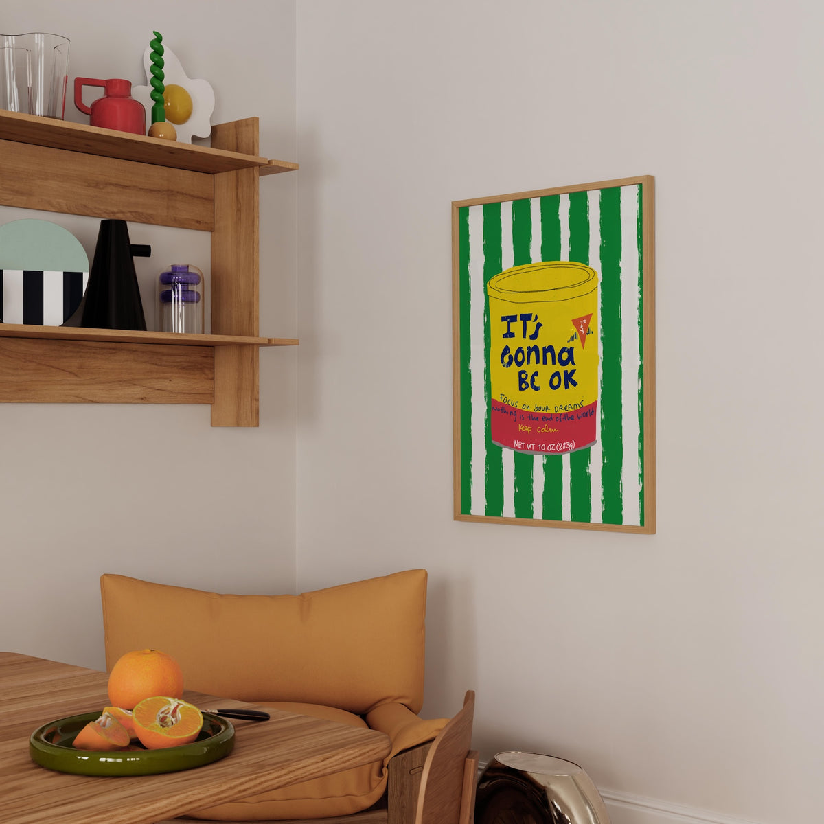 Framed artwork on a wall above a wooden chair with a table and oranges.