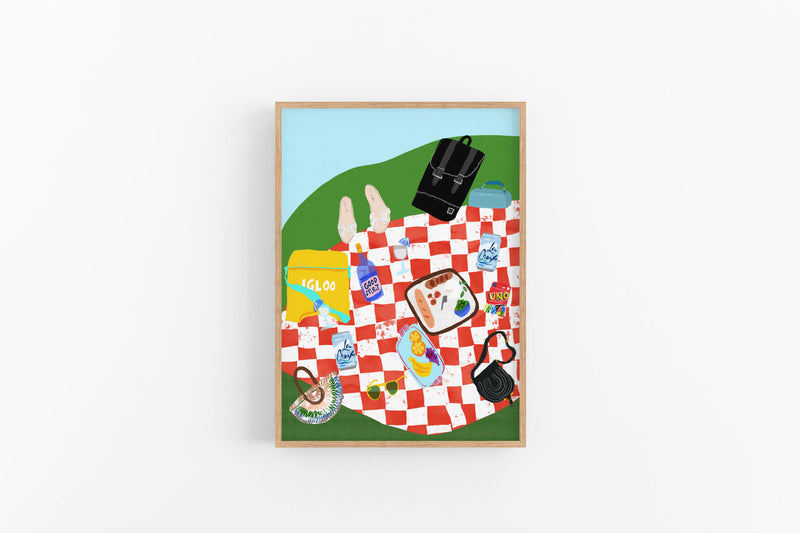 Vibrant art print of a red checkered picnic blanket with an Igloo cooler, Uno cards, wine, and fruit. Bold summer-themed wall decor.