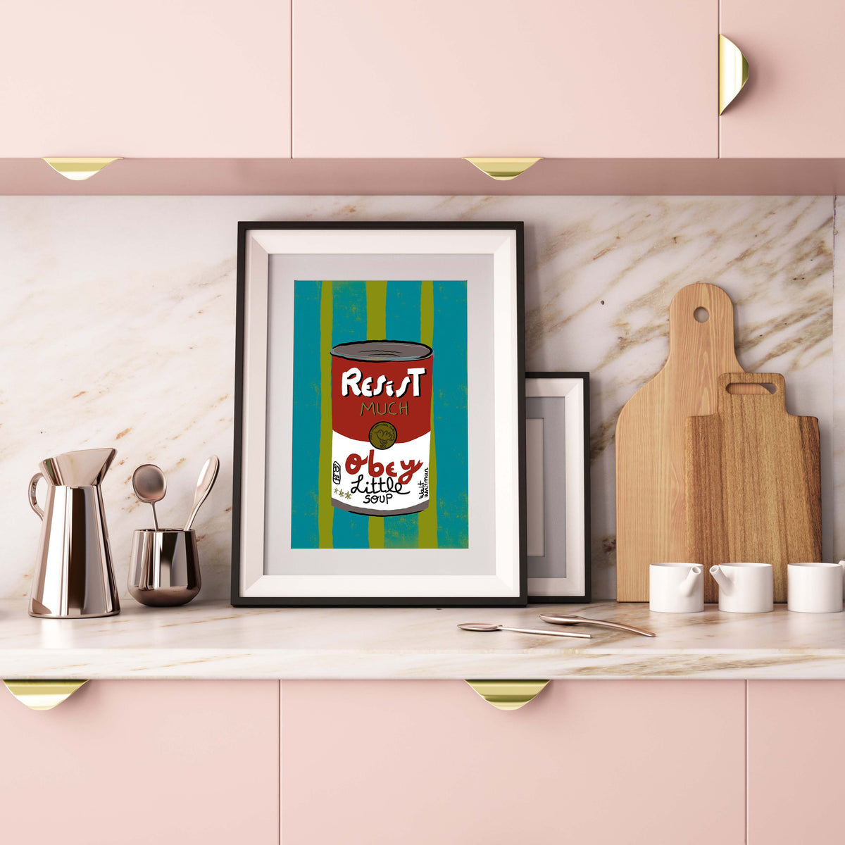 Framed artwork on a kitchen counter with pink cabinets and marble backsplash.