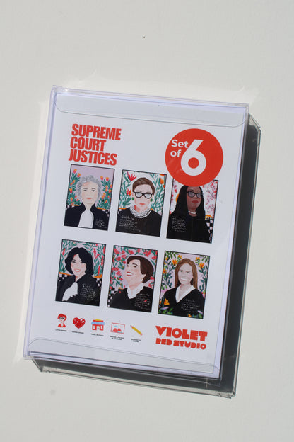 A clear plastic sleeve encloses a printed card or booklet titled 'Supreme Court Justices Set of 6' with six illustrated portraits and 'Violet Red Studio' branding, photographed on a plain light background.