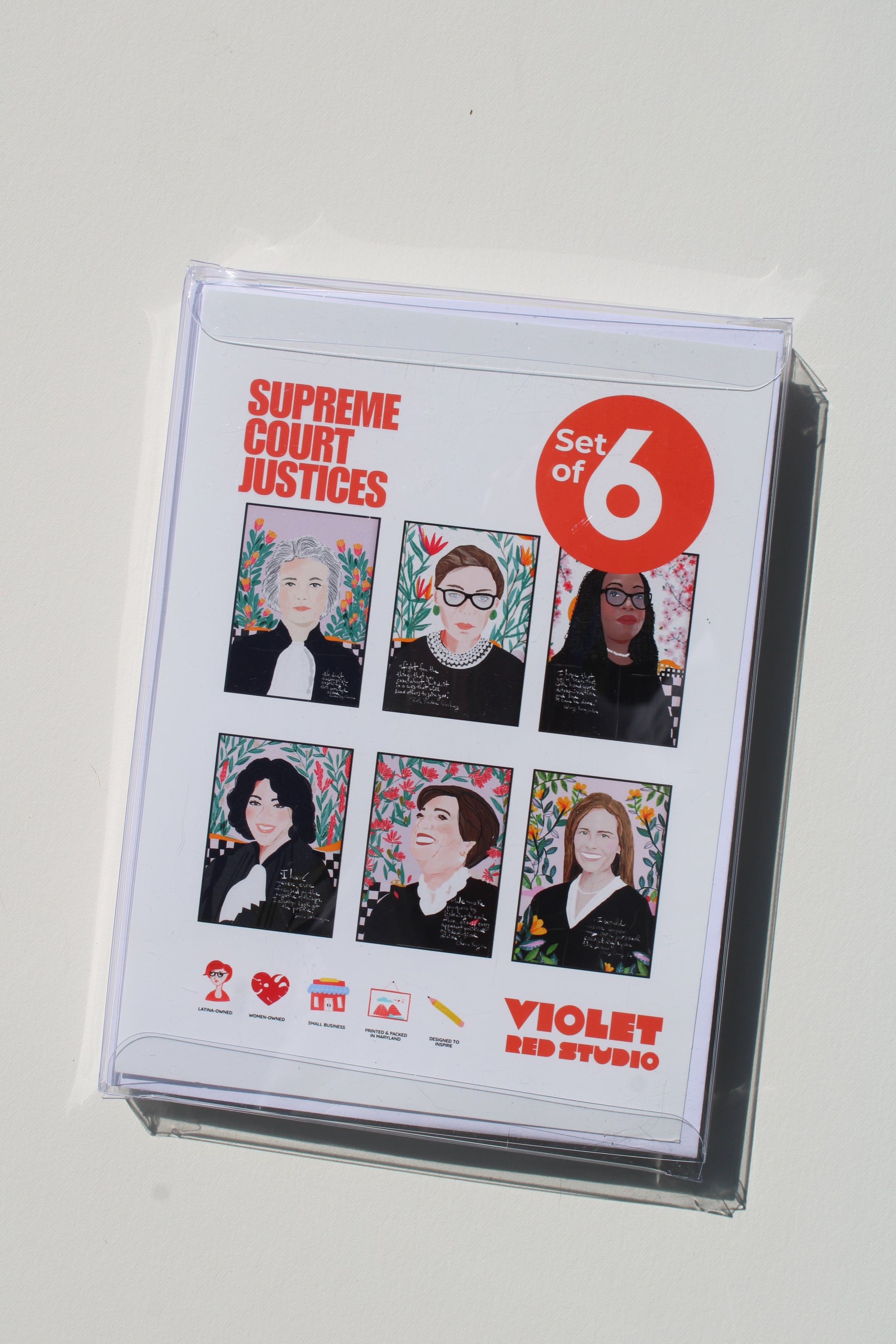 A clear plastic protective case holding a printed card or booklet titled 'Supreme Court Justices' with 'Set of 6' in a red circle, featuring six illustrated portraits and 'Violet Red Studio' branding, photographed on a plain light background.