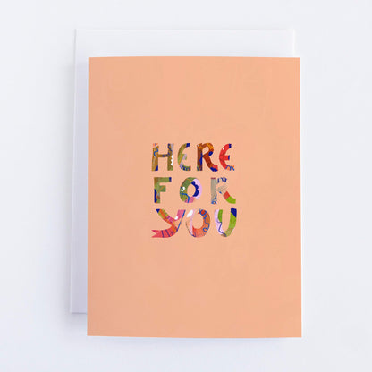 A greeting card with 'HERE FOR YOU' printed in multicolored letters on a peach-colored background, with a white envelope included.