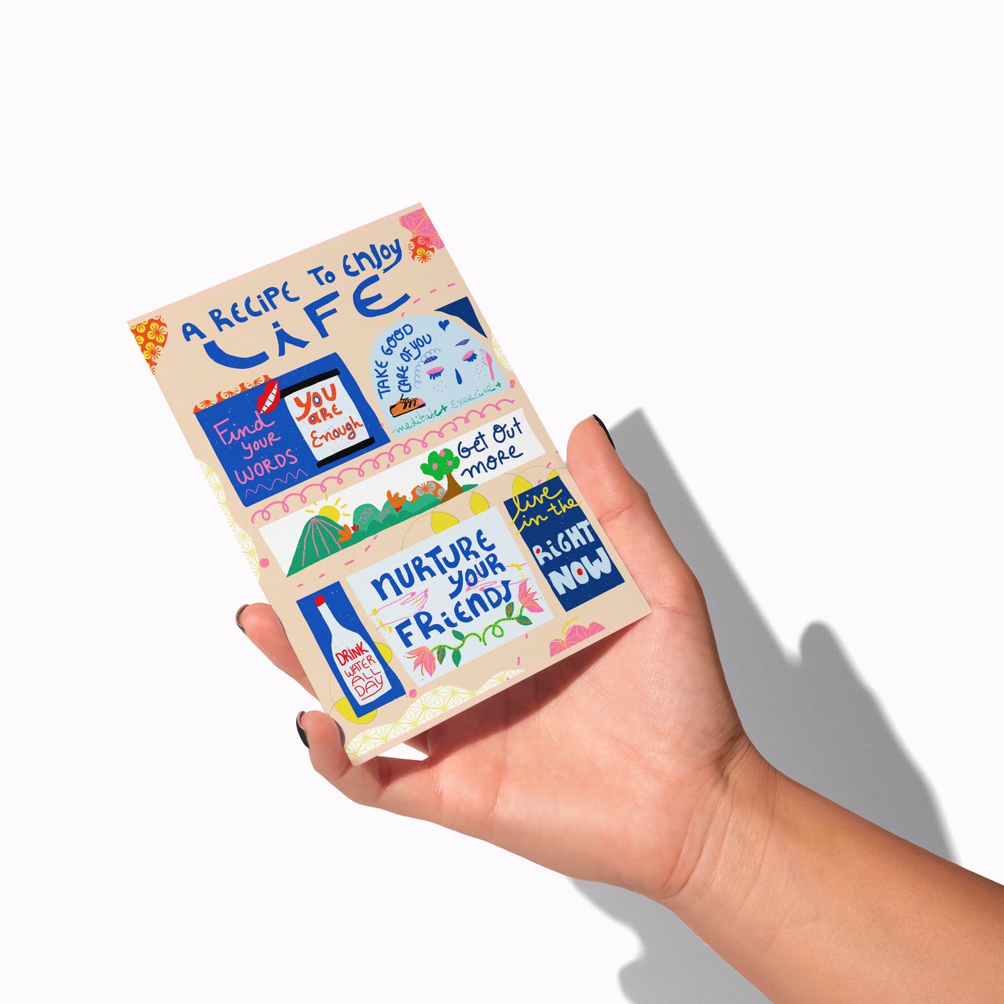 Hand holding a colorful book titled 'A Recipe to Enjoy Life' with various sayings on a white background.