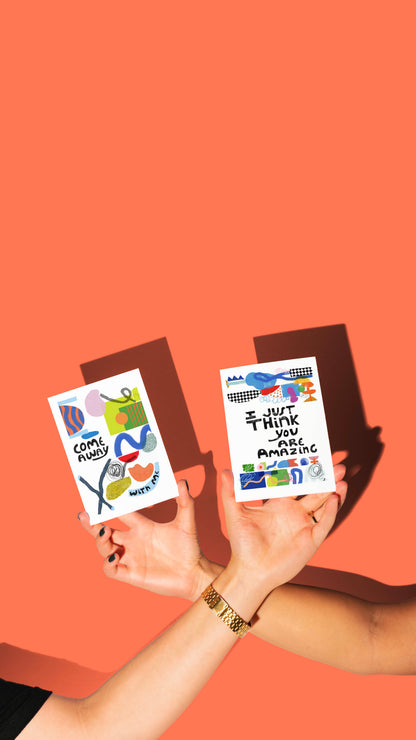 Two hands holding colorful greeting cards against an orange background
